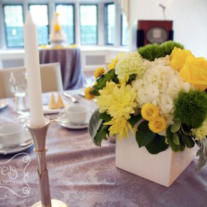 Fresh yellow roses, yellow cushion mums, green trick dianthus, light green carnations, succulents, cream hydrangea, yellow button mums, and dusty miller, in white cube pot