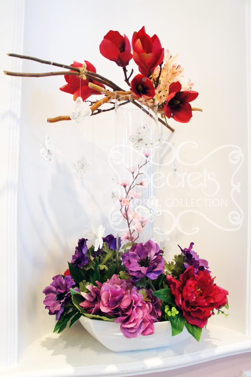 Artificial red mangolia, pink eremurus, pink cherry blossoms, fuchsia peonies, purple hydrangea, and purple anemones centrepiece with suspending butterflies (overview)