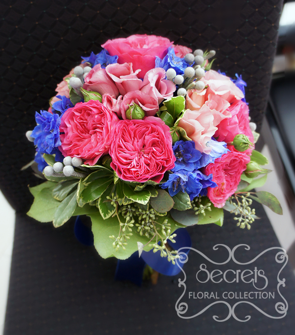 Fresh fuchsia garden roses, medium pink lisianthus,dark blue delphinium, silver brunia berries, and green seeded eucalyptus bridal bouquet, with a royal blue and sparkly mesh wrap (front-view) - Toronto Wedding Flowers by Secrets Floral Collection