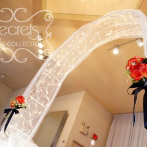 Wedding Arch, Decorated with Twinkle Lights, White Tulle, and Red Bouquet Pull-Backs