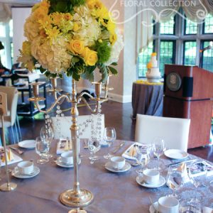 Elevated centrepiece with fresh yellow roses, yellow cushion mums, green trick dianthus, light green carnations, succulents, cream hydrangea, yellow button mums, and dusty miller, on chrome candelabra with crystal strands