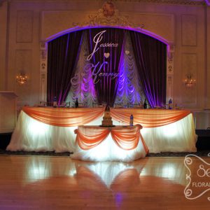 Head and cake tables with cream chiffon skirting, peach satin swags, and large crystal buckles - Toronto Wedding Decor Created by Secrets Floral Collection