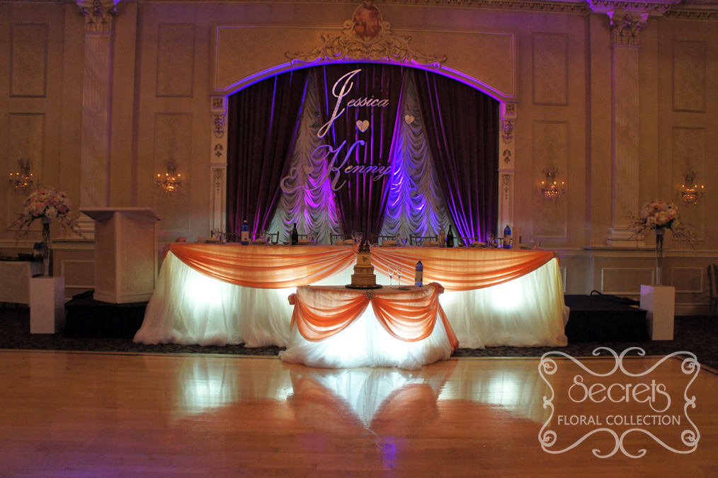 Head and cake tables with cream chiffon skirting, peach satin swags, and large crystal buckles - Toronto Wedding Decor Created by Secrets Floral Collection