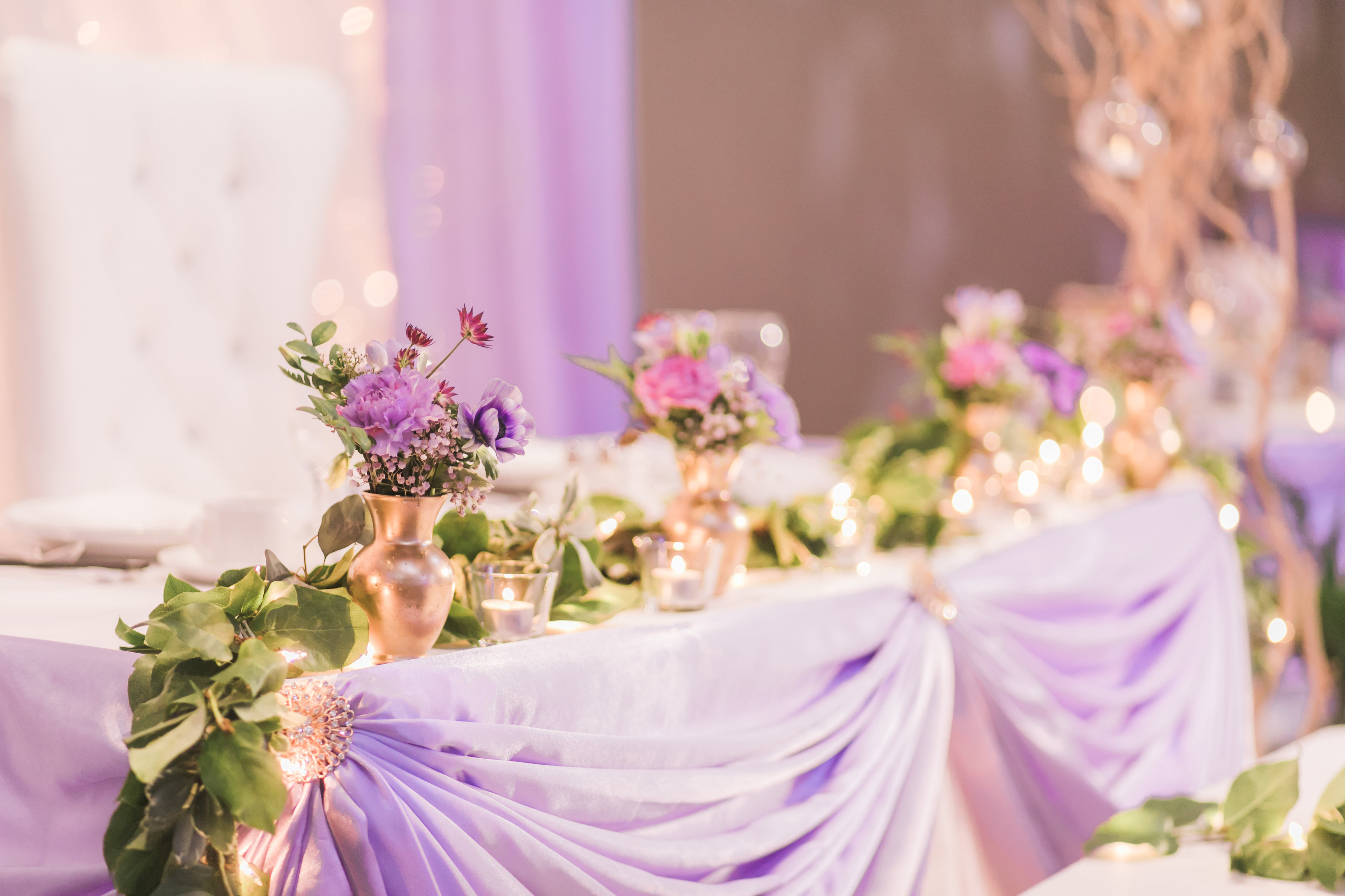 Wedding reception, with twinkle lights backdrop, and lavender head table. Purple flowers in gold bud vases. Toronto wedding flowers and decor at Fontana Primavera by Secrets Floral.