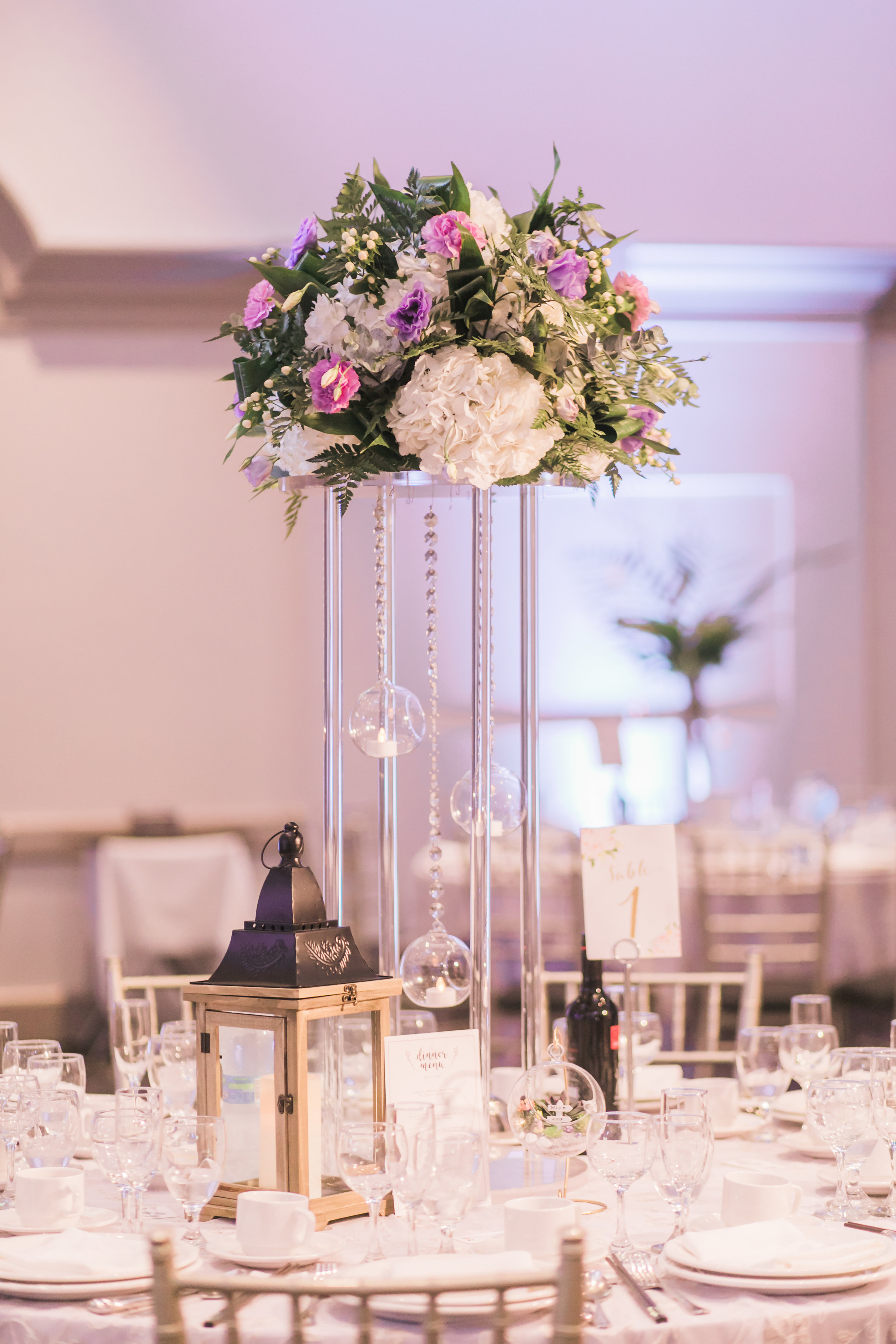Fresh tall floral centrepiece arrangement, with cream hydrangea, purple lisianthus, and greenery. Suspending glass globes and rustic lantern at side. Toronto wedding flowers and decor at Fontana Primavera by Secrets Floral.